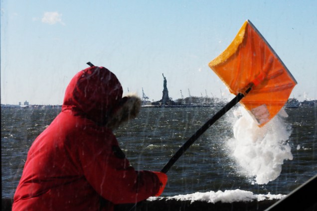 Homem retira neve com pá próximo ao rio Hudson e da Estátua da Liberdade, durante onda de frio que atinge o estado americano de Nova York - 06/01/2017