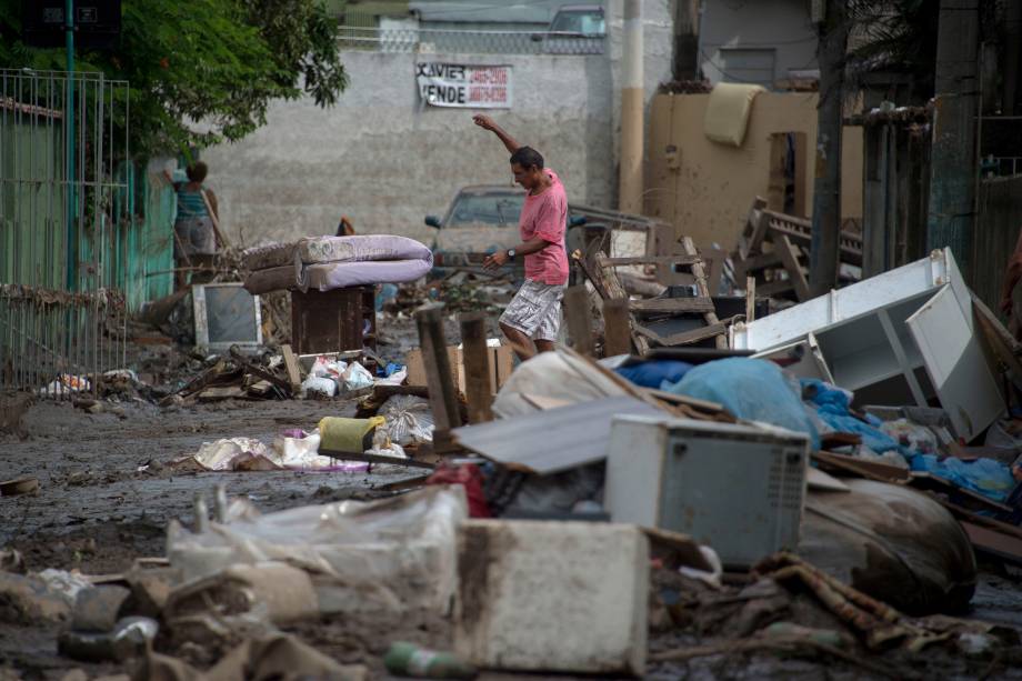 Homem caminha em uma rua coberta de móveis destruídos após enchentes que espalharam lama e estragos no bairro de Bonsucesso, no Rio de Janeiro - 15/02/2018