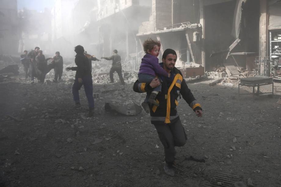 Homem carrega uma criança ferida em bombardeios do governo na cidade rebelde de Hamouria, na região sitiada de Ghouta Oriental, nos arredores da capital Damasco - 19/02/2018