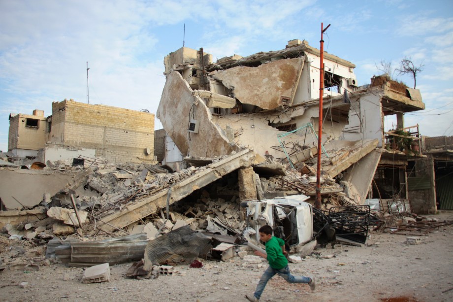 Menino corre em frente a edifício completamente destruído durante ataques aéreos das forças do regime sírio na cidade rebelde de Douma, na região sitiada de Ghouta Oriental - 20/02/2018