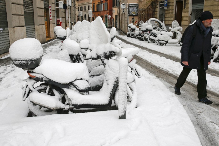 Um homem caminha ao lado de um estacionamento, onde todas as motocicletas estão cobertas de neve, devido a uma onda de frio que congelou a cidade de Roma, na Itália - 26/02/2018