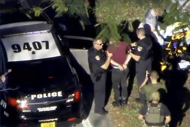 Homem algemado é conduzido para viatura por policiais, após tiroteio em uma escola de Parkland, Flórida