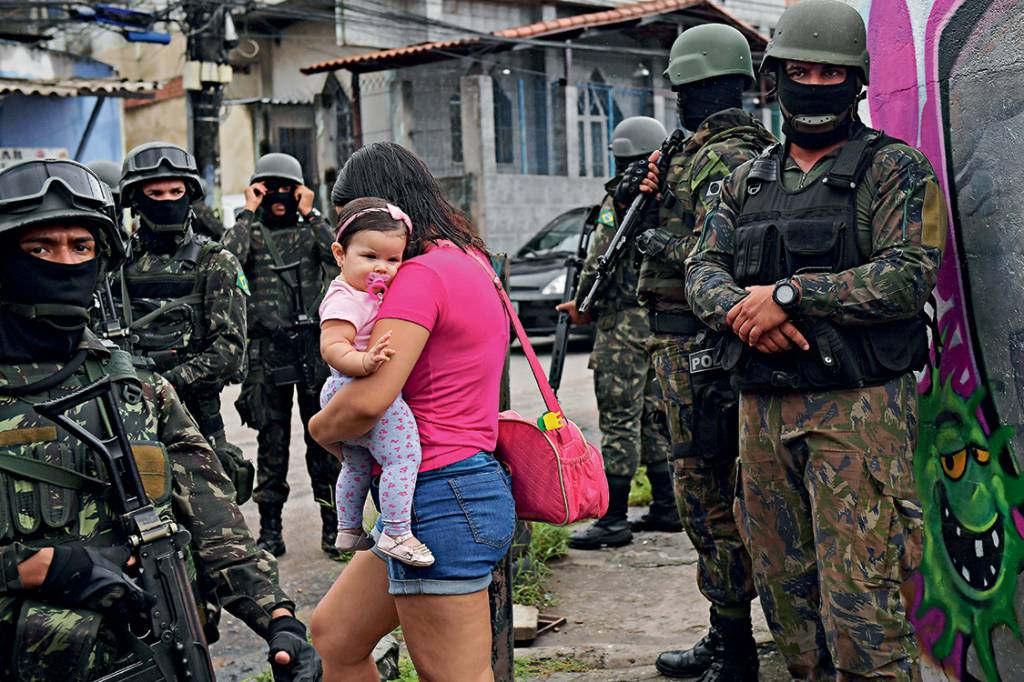 Sob intervenção - Moradora da Vila Kennedy, no Rio, passa pelos soldados: a população das favelas no meio da guerra