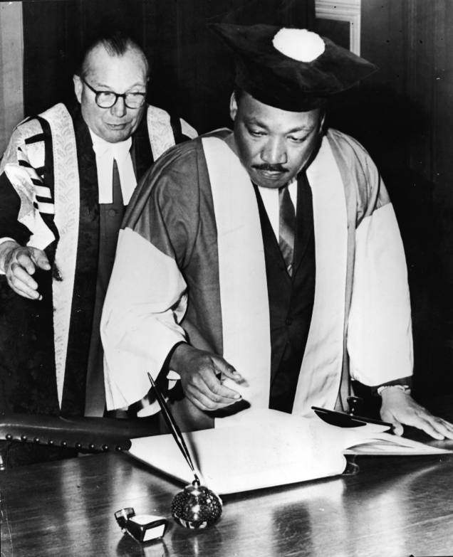 Martin Luther King, Jr., assistido pelo Dr. Charles Bousenquet, assina o curso de graduação na Universidade de Newcastle depois de receber um título honorário de Doutor em Direito Civil, na Inglaterra - 14/11/1967