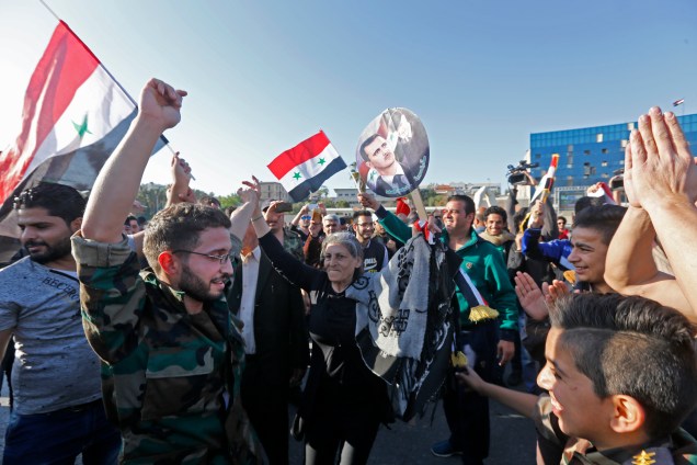 Manifestantes sírios agitam bandeiras e seguram  retratos do presidente Bashar al-Assad, enquanto se reúnem na Praça Umayyad, em Damasco, para reivindicar o bombardeio realizado pelos Estados Unidos, Reino Unido e França - 14/04/2018