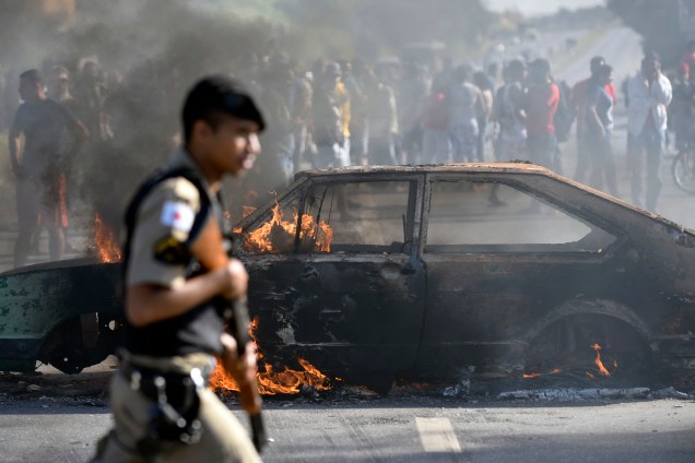 Policial passa por um carro incendiado por manifestantes que protestam contra os preços dos combustíveis no bairro de São Marino, em Ribeirão das Neves, região metropolitana de Belo Horizonte (MG) - 25/05/2018