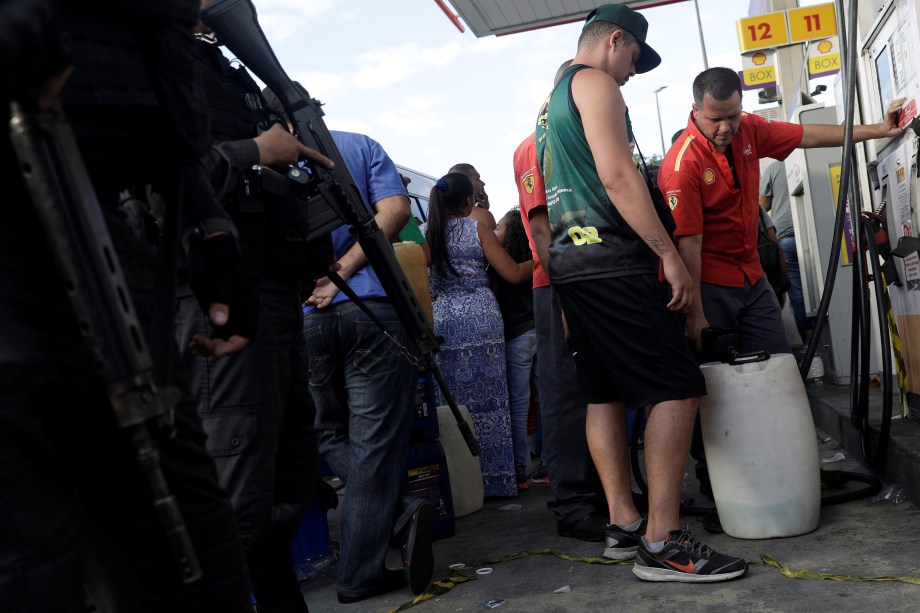 Policiais patrulham enquanto pessoas enchem vasilhas com gasolina em um posto de combustível no Rio de Janeiro - 28/05/2018