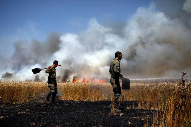 Soldados israelenses tentam extinguir um incêndio em um campo no lado israelense da fronteira entre Israel e Gaza, perto do kibutz Mefalsim - 14/05/2018
