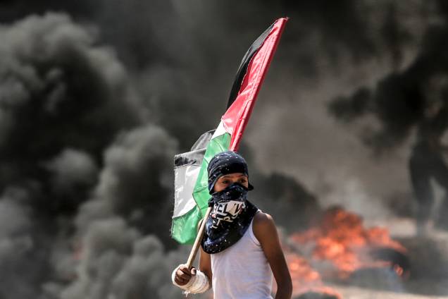 Menino Palestino segura bandeira durante confronto com tropas Israelenses na Faixa de Gaza - 14/05/2018