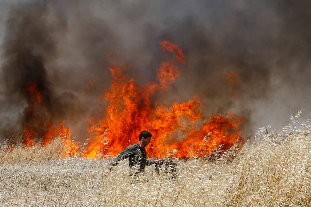 Soldado Israelense tenta apagar fogo em plantação de trigo causado por manifestantes na Faixa de Gaza - 14/05/2018