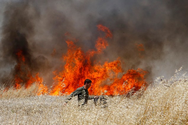 Soldado Israelense tenta apagar fogo em plantação de trigo causado por manifestantes na Faixa de Gaza - 14/05/2018