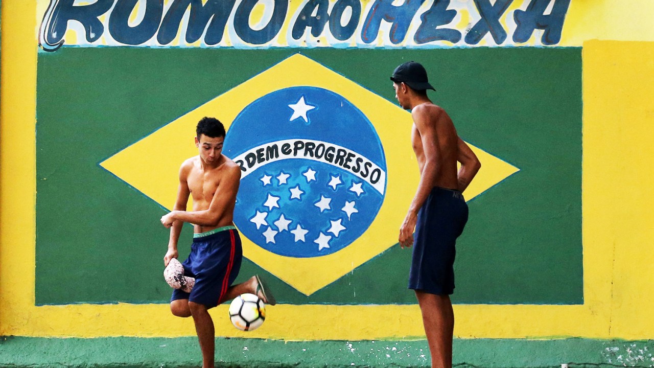Moradores jogam futebol próximos de mural com a bandeira do Brasil, no Rio de Janeiro (RJ), às vésperas da Copa do Mundo da Rússia - 12/06/2018