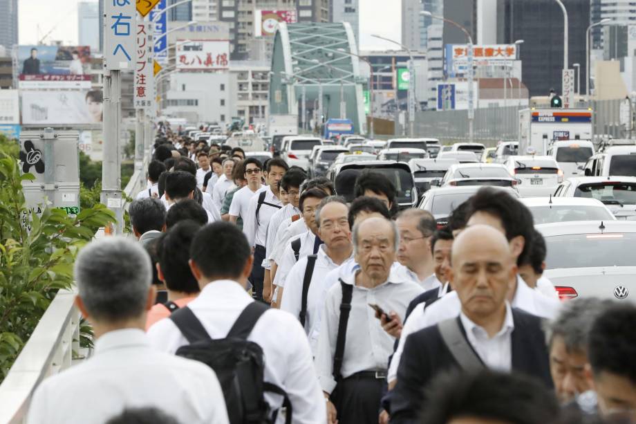 Pessoas andam em uma ponte sobre o rio de Yodo depois que os serviços de transporte público foram suspensos para verificações de dano após um terremoto em Osaka, no Japão - 18/06/2018