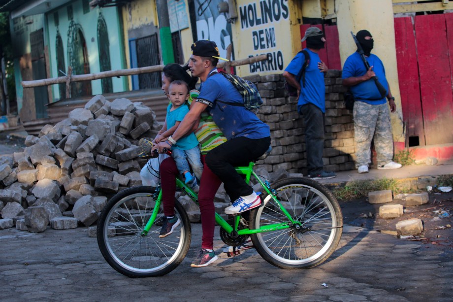 Família passa de bicicleta por manifestantes pró-governo após confrontos na comunidade indígena de Monimbo, em Masaya, Nicarágua - 17/07/2018