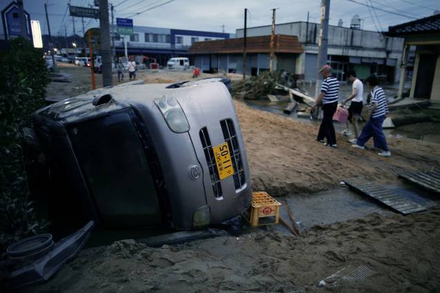 Moradores caminham ao lado de um carro danificado em uma área inundada em Kurashiki, província de Okayama, Japão - 08/07/2018