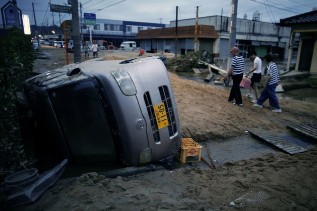 Moradores caminham ao lado de um carro danificado em uma área inundada em Kurashiki, província de Okayama, Japão - 08/07/2018