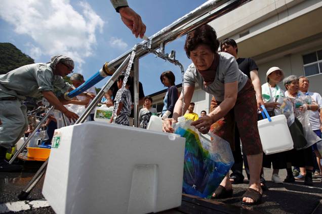 Moradores recebem água perto de uma área inundada na escola secundária Mihara Daini, que tem servido como uma estação de abastecimento de emergência, em Mihara, prefeitura de Hiroshima, no Japão - 09/07/2018