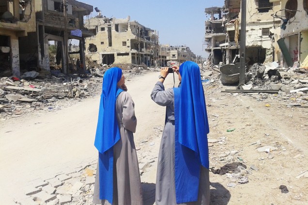 Duas freiras fotografam área destruída por bombardeios de Israel.