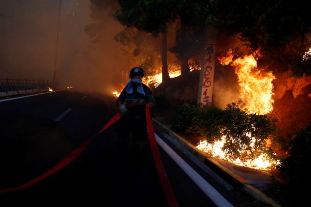 Soldado segura uma mangueira enquanto um incêndio florestal avança sobre a cidade de Rafina, perto de Atenas, na Grécia - 23/07/2018