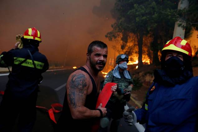 Bombeiros, soldados e moradores carregam uma mangueira enquanto um incêndio florestal atinge a cidade de Rafina, perto de Atenas, na Grécia - 23/07/2018