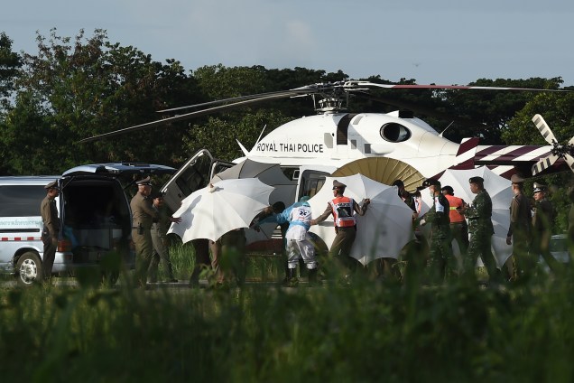 Policiais e militares usam guarda-chuvas para cobrir uma maca perto de um helicóptero e uma ambulância no aeroporto militar em Chiang Rai, durante operação de resgate dos meninos presos em um caverna no norte da Tailândia - 09/07/2018