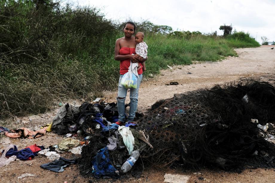 A venezuelana Joanna e seu filho Bruno, do estado de Anzoátegui, posam ao lado de seus pertences queimados por civis brasileiros, enquanto segura um pacote com fraldas doadas no controle de fronteira de Pacaraima, em Roraima - 19/08/2018