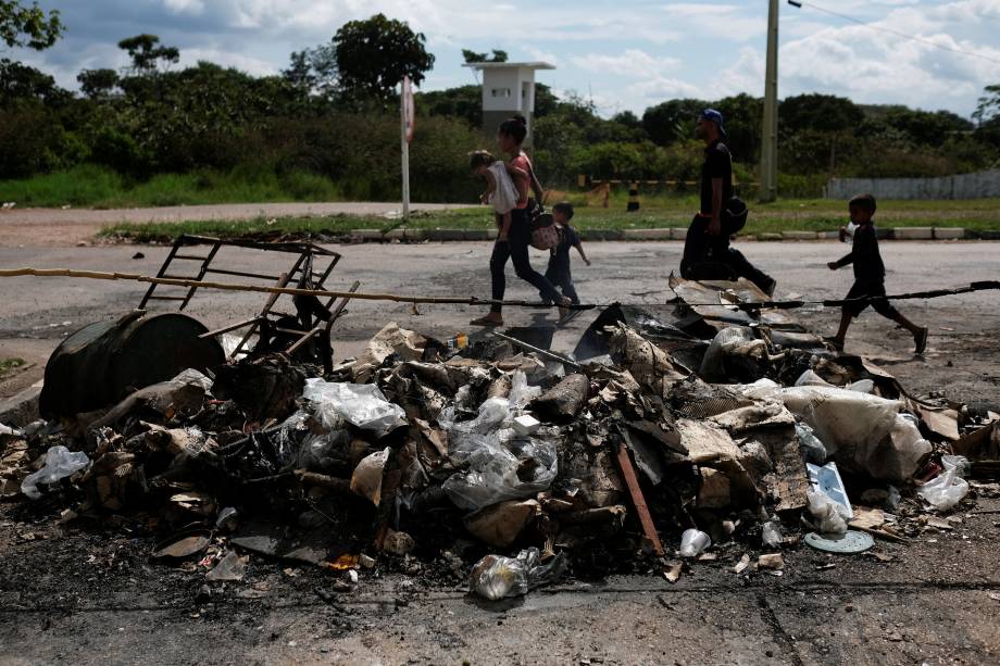 Venezuelanos passam por pertences e barracas queimadas por civis brasileiros no controle de fronteira de Pacaraima, em Roraima - 19/08/2018