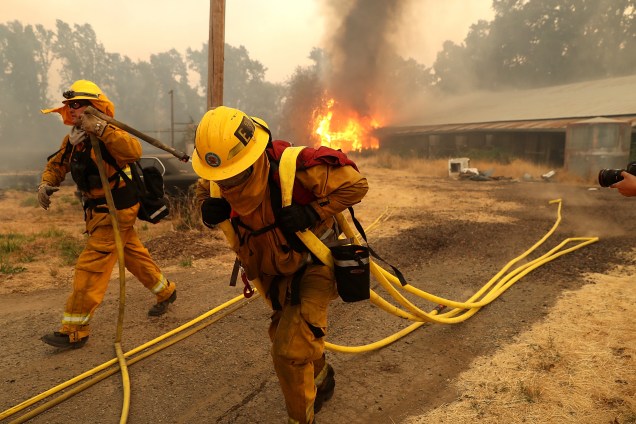 Bombeiros carregam mangueiras enquanto um celeiro arde nas chamas do incêndio River Fire em Lakeport, na Califórnia - 01/08/2018
