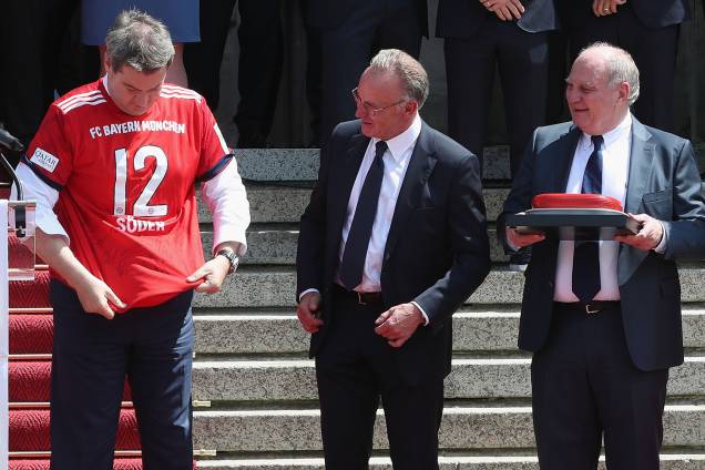 O governador da Baviera, Markus Söder (esq), é visto com camiseta do Bayern de Munique, juntamente com o CEO do clube, Karl-Heinz Rummenigge, e o presidente do Conselho de Administração Uli Hoeness - 09/05/2018