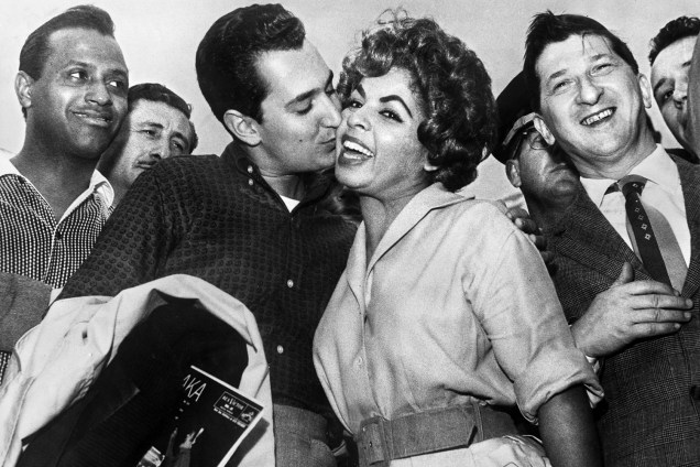 O cantor e compositor americano Neil Sedaka beija a cantora brasileira Ângela Maria, observado pelo cantor Carlos Gonzaga em São Paulo - 08/11/1959