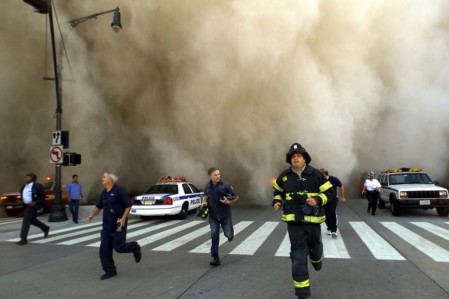 Policiais e bombeiros correm de uma enorme nuvem de fumaça no momento da queda de uma das torres do World Trade Center - 11/09/2001