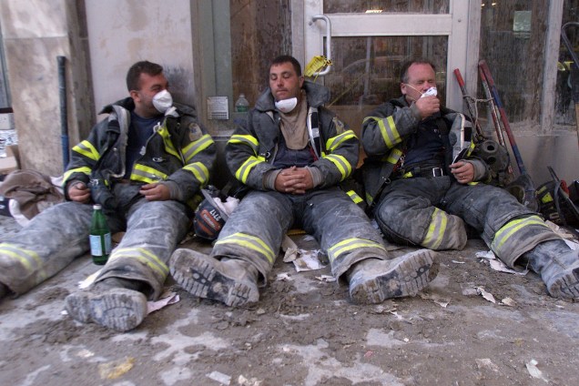 Bombeiros exaustos descansam na Broadway durante a busca por sobreviventes após atentado terrorista no World Trade Center - 11/09/2001
