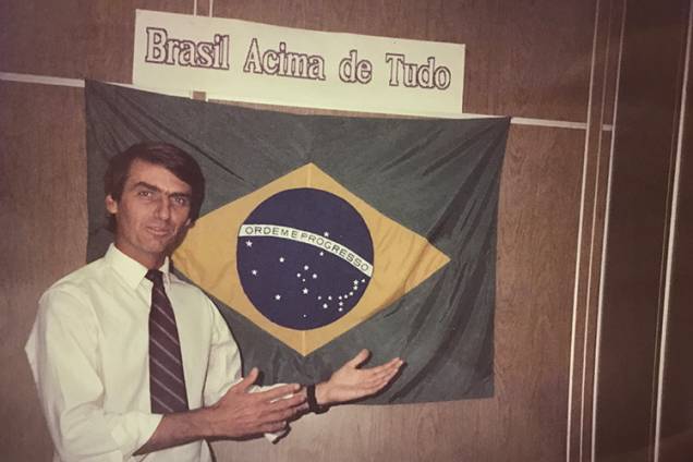 Jair Bolsonaro posa para foto com a bandeira do Brasil na frente de seu gabinete na Câmara dos Deputados