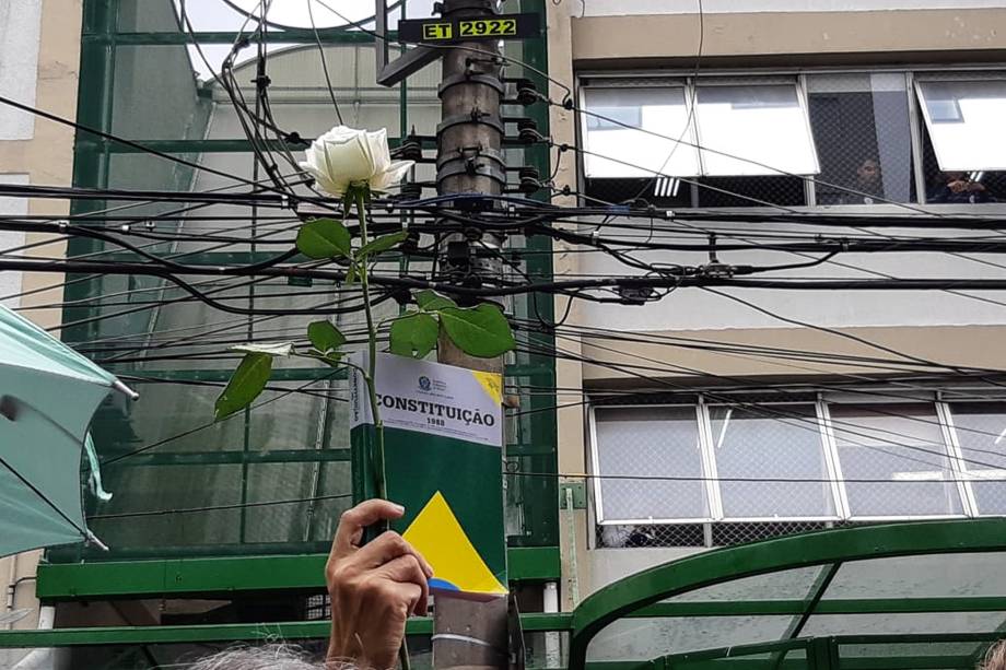 Apoiador de Fernando Haddad ergue um botão de rosa junto com um exemplar da Constituição em frente ao local de votação do candidato do PT à Presidência da República, em São Paulo