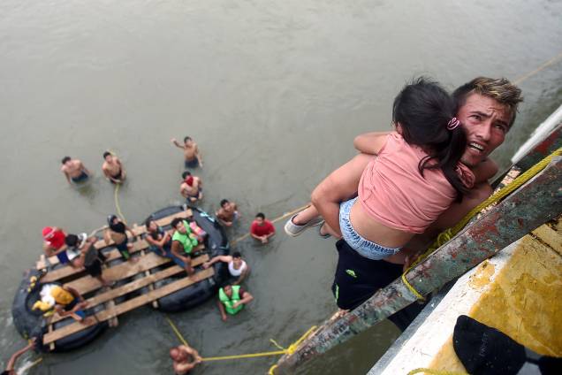 Imigrante hondurenho segura uma criança ao descer de uma ponte que liga México e Guatemala para evitar o posto fronteiriço em Ciudad Hidalgo, no México - 20/10/2018