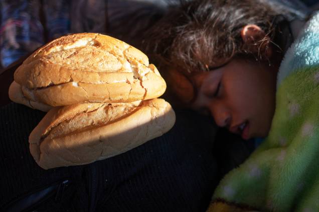 Garota dorme próxima de pão que foi doado para imigrantes hondurenhos, nos arredores da cidade mexicana de Tapachula - 22/10/2018
