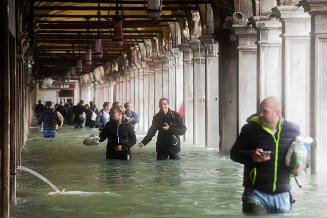 Com água na região da cintura, pedestres andam pelos arcos da Praça de São Marcos, em Veneza, na Itália - 29/10/2018