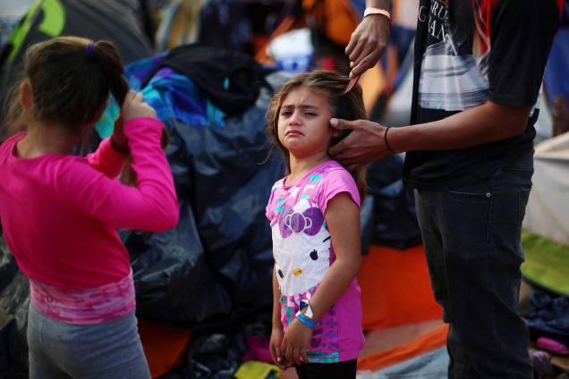 Garota chora enquanto seu pai escova seu cabelo em acampamento improvisado, montado por membros da caravana de imigrantes da América Central, nos arredores da fronteira entre o México e os Estados Unidos, na cidade de Tijuana - 28/11/2018