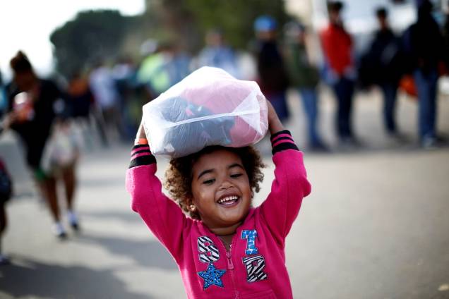 Menina hondurenha, parte da caravana de milhares de pessoas que viajam a caminho dos Estados Unidos, sorri enquanto carrega roupas doadas em um abrigo da cidade mexicana de Tijuana - 21/11/2018