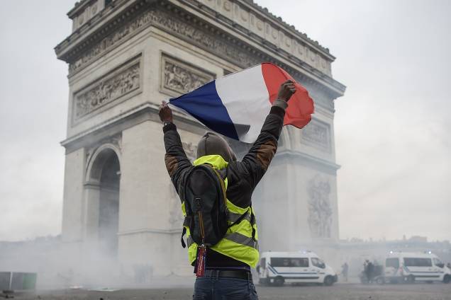 Manifestante segura uma bandeira francesa em meio a fumaça de gás lacrimogêneo lançado pela polícia em frente do Arco do Triunfo, na Champs Elysees, em Paris durante uma manifestação nacional contra o aumento dos preços do petróleo e do custo de vida - 24/11/2018