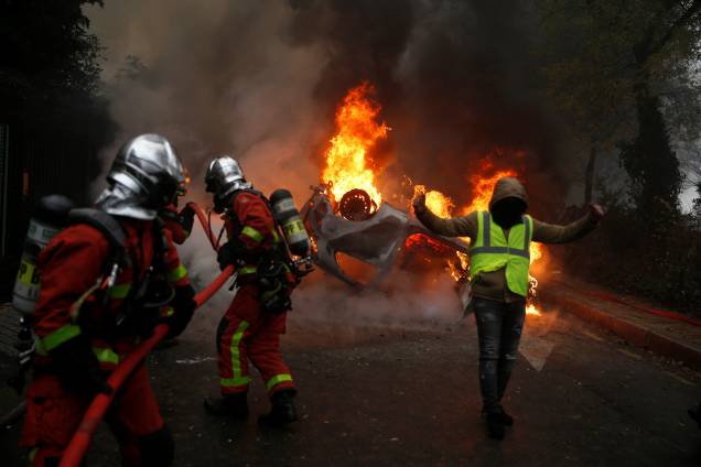 Manifestantes vestindo coletes amarelos, um símbolo de um protesto de motoristas franceses contra impostos mais elevados sobre o diesel, passa perto de um carro em chamas durante os protestos perto da Place de l'Etoile em Paris, França - 01/12/2018