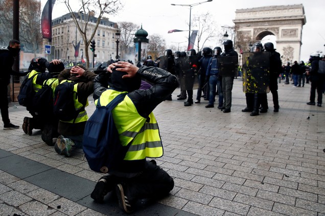 Manifestantes com coletes amarelos se ajoelham na Avenida Champs-Élysées próximo ao Arco do Triunfo e encara a Polícia francesa em Paris, França - 08/12/2018
