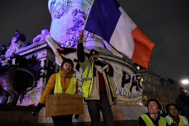 Manifestantes com coletes amarelos exibem cartazes e a bandeira da França durante protesto na Praça da República em Paris, França - 08/12/2018