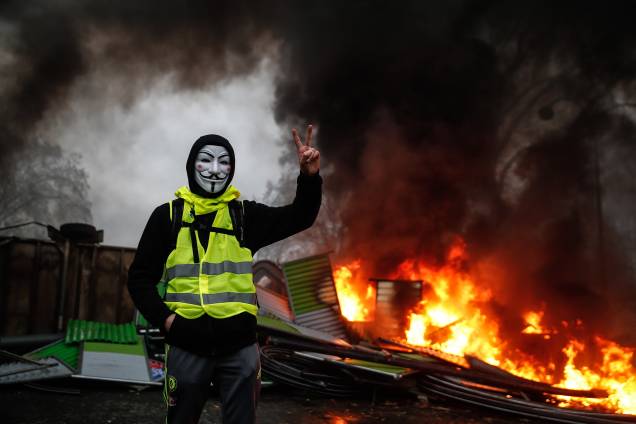 Manifestante usa uma máscara de Guy Fawkes perto de uma barricada em chamas durante protesto dos coletes amarelos (Gilets jaunes) contra o aumento dos preços do diesel e do custo de vida em Paris - 01/12/2018