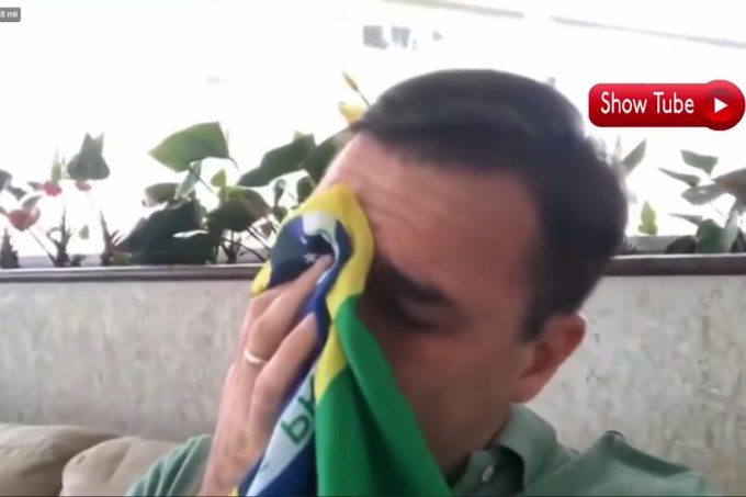 Flavio Bolsonaro enxuga as lágrimas com uma bandeira do Brasil ao falar do pai