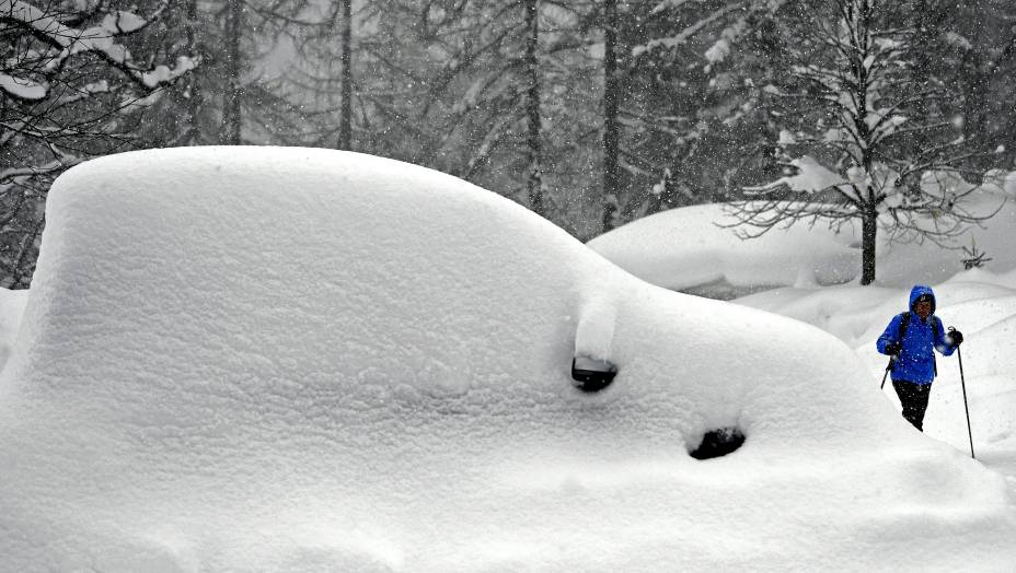 Mulher passa ao lado de um carro coberto pela neve em Ramsau am Dachstein, na Áustria - 08/01/2019