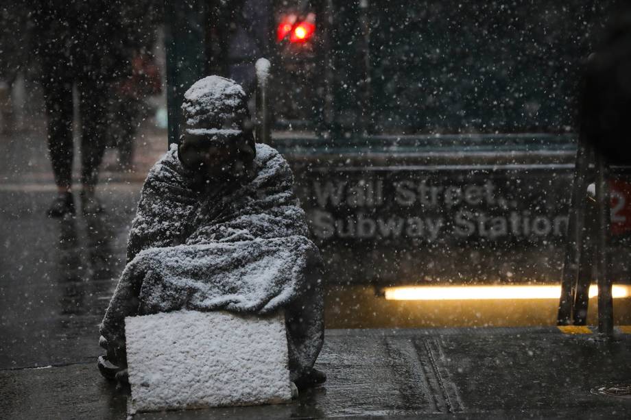 Morador de rua é coberto de neve enquanto fica sentado ao lado da estação Wall Street do metrô de Nova York - 30/01/2019