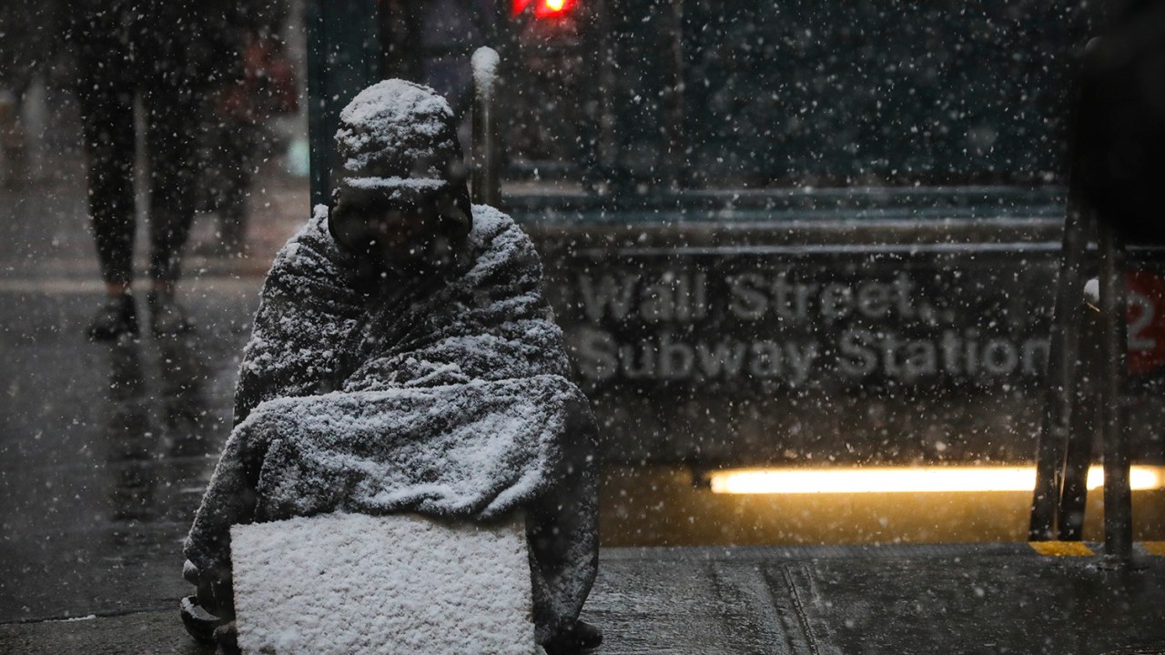 Morador de rua é coberto de neve enquanto fica sentado ao lado da estação Wall Street do metrô de Nova York - 30/01/2019