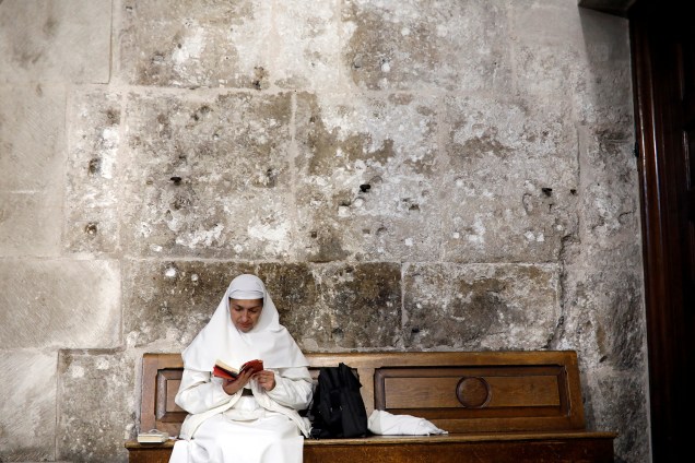 Freira lê sentada em banco dentro da Igreja do Santo Sepulcro na Cidade Velha de Jerusalém - 17/11/2018