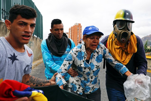 Manifestantes se protegem de bombas de gás lacrimogêneo lançadas por policiais, durante marcha contra o presidente venezuelano Nicolás Maduro, em Caracas - 23/01/2019